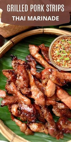 grilled pork strips on a banana leaf with dipping sauce