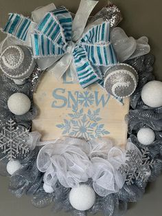 a christmas wreath with snow decorations and ribbons on the front door, hanging on a wall