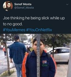 a young boy standing next to a pole on the side of a road with an orange and blue jacket