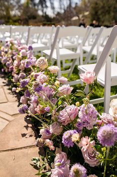 rows of white chairs with purple and pink flowers lining the side of each chair for an outdoor ceremony