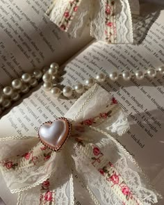 an open book with pearls, lace and a heart shaped brooch on the pages