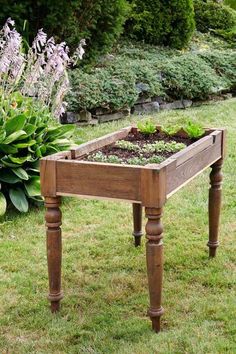 an old wooden table with plants in it on the grass near some bushes and flowers