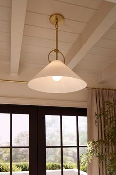 a light fixture hanging from the ceiling in a room with large windows and potted plants