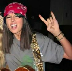 a woman holding a guitar and wearing a red bandana with her hands in the air