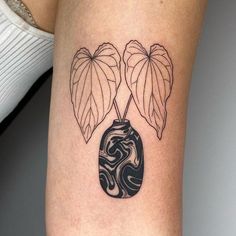 a woman's leg with a tattoo on it that has two leaves and a vase