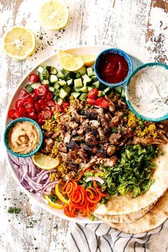 a white plate topped with meat and veggies next to pita breads