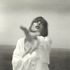 a black and white photo of a woman with her hands out in the air while standing near the ocean