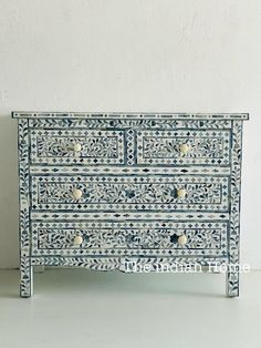 an ornate blue and white chest of drawers with knobs on each drawer, in front of a wall