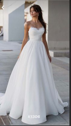 a woman in a white wedding dress standing on the sidewalk