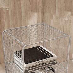 a metal wire basket holding several books on top of a wooden floor next to a wall