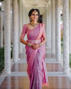 a woman in a pink sari standing on a wooden floor with columns behind her