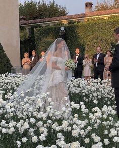 the bride and groom are standing in front of white flowers, surrounded by other people