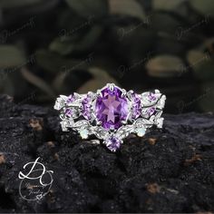 an amethoraite and diamond ring sitting on top of a black rock with leaves