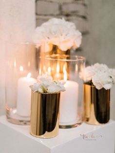 three gold and white vases filled with flowers on top of a table next to candles