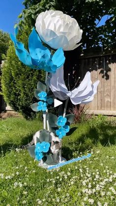 a sculpture made out of paper flowers in the middle of a yard with grass and white daisies