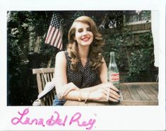 a woman sitting at a table with an american flag in the background, holding a soda bottle