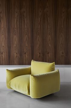 a yellow chair sitting in front of a wall with wood paneled walls behind it