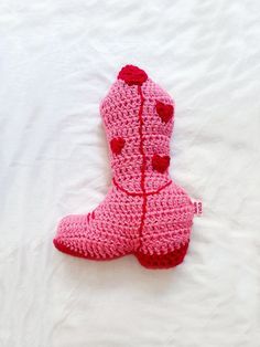 a crocheted pink boot is laying on a white sheet and has red hearts