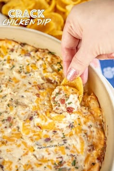 a hand dipping a tortilla chip into a cheesy dip in a casserole dish