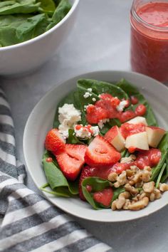 a white bowl filled with spinach and strawberries next to a glass of strawberry juice