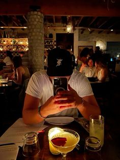 a man sitting at a table taking a selfie with his cell phone in front of him