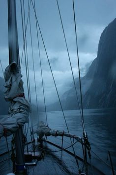 the back end of a sailboat on a body of water with mountains in the background