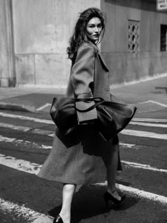 black and white photograph of woman in coat crossing street with handbag on her hip