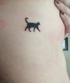 a small black cat tattoo on the side of a woman's stomach and chest