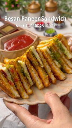 a person holding a plate with sandwiches on it and dipping sauces in the background