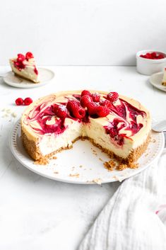 a cheesecake with raspberries is on a plate and has one slice cut out