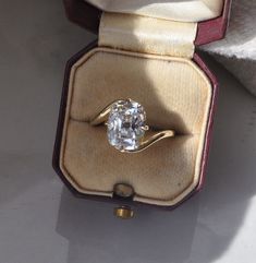 an oval cut diamond sits in a velvet ring box, with the lid open to show it's inside