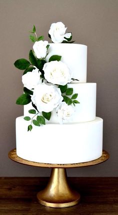 a three tiered cake with white flowers on top and green leaves on the bottom