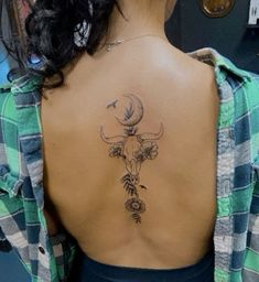 the back of a woman's neck with a deer skull and flowers on it