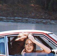 a woman sitting in the passenger seat of a red car with her hand on her head