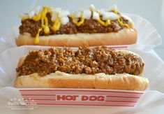 two chili dogs in buns with mustard and ketchup on the top one