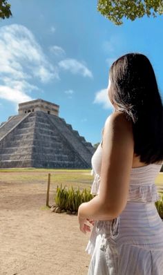 a woman in a white dress looking up at an ancient pyramid on a sunny day