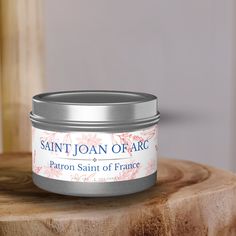 a jar of saint joan of arc sits on a wooden table next to a candle