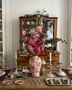 a dining room table with plates, cups and flowers in vases on it's centerpiece