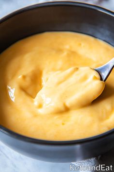 a spoon full of yellow sauce in a black bowl on a white tablecloth with a silver spoon