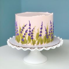 a decorated cake sitting on top of a white plate covered in frosting and purple flowers