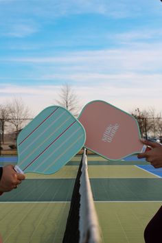 two people holding up paddles on top of a tennis court with the sky in the background