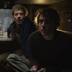 two men sitting on a couch in the dark