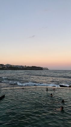 people are swimming in the ocean at sunset