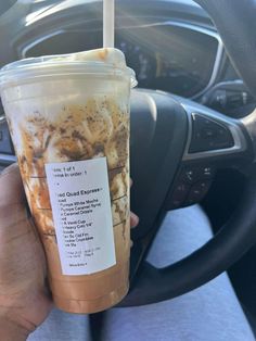 a person holding up a drink in their hand and steering wheel behind the cup is an information card