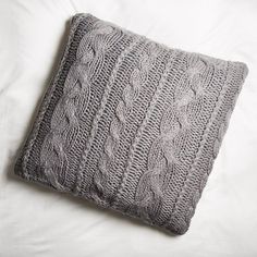 a gray knitted pillow sitting on top of a bed