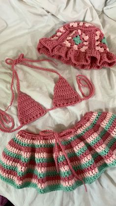 two crocheted bikinisuits on a bed next to a hat and purse