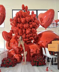 a woman standing in front of giant red heart shaped balloons with roses on the floor