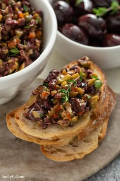 two bowls filled with food sitting on top of a table next to bread and grapes