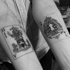 two people with matching tattoos on their arms holding playing cards in front of each other