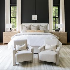 a bedroom with black walls and white bedding, two chairs in front of the bed